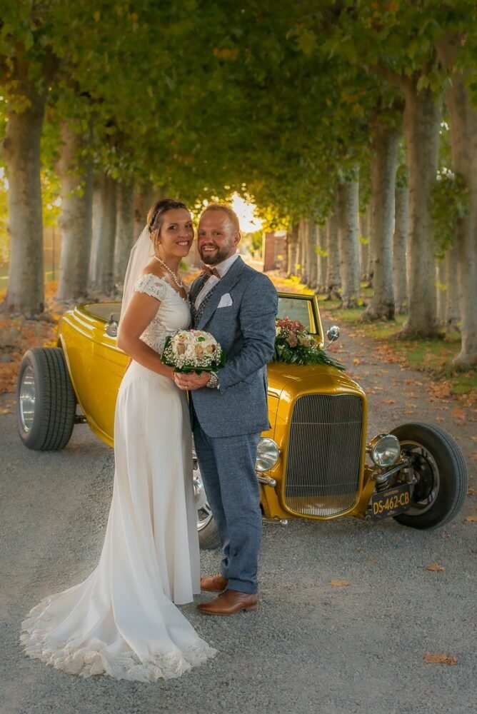 Des mariés debout à côté d’une voiture hot rod jaune pour leur séance photo de mariage à Perpignan.