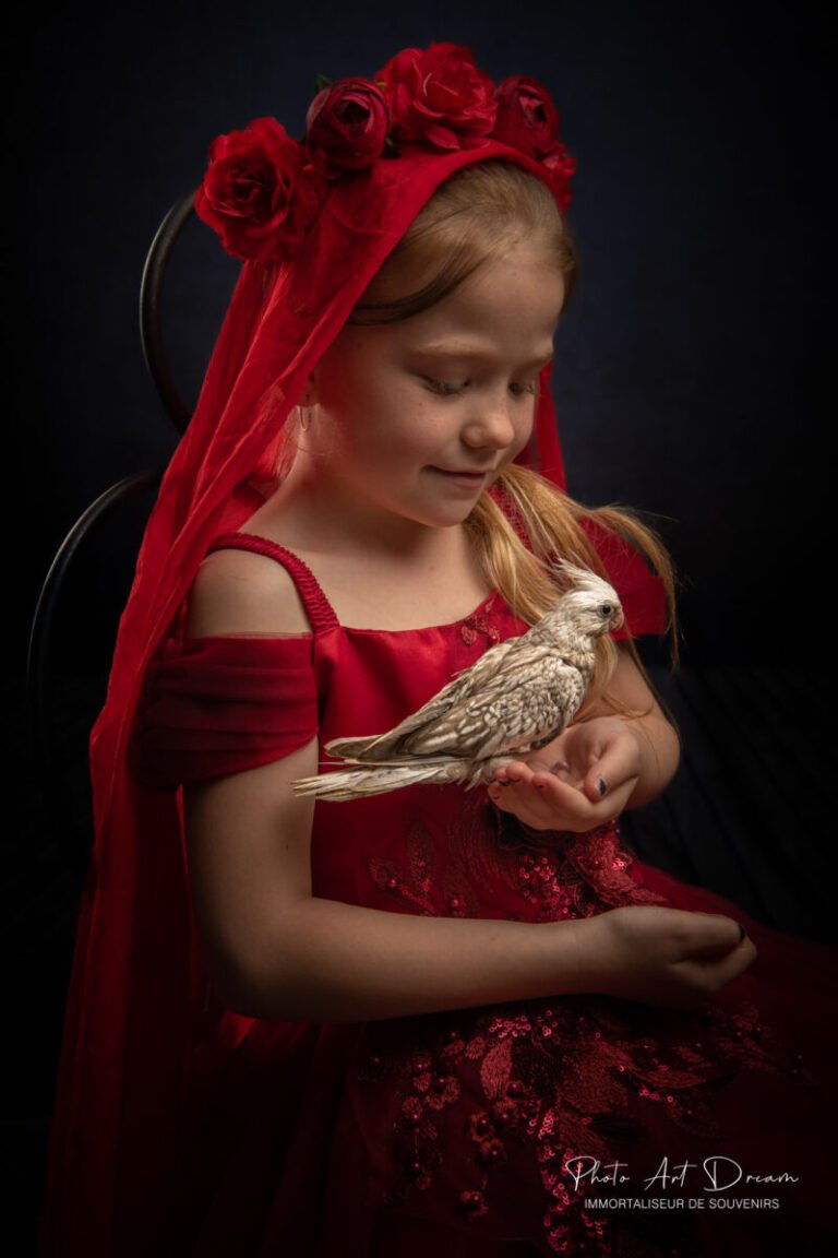 Une petite fille en robe rouge tenant un oiseau capturé dans un portrait de famille.